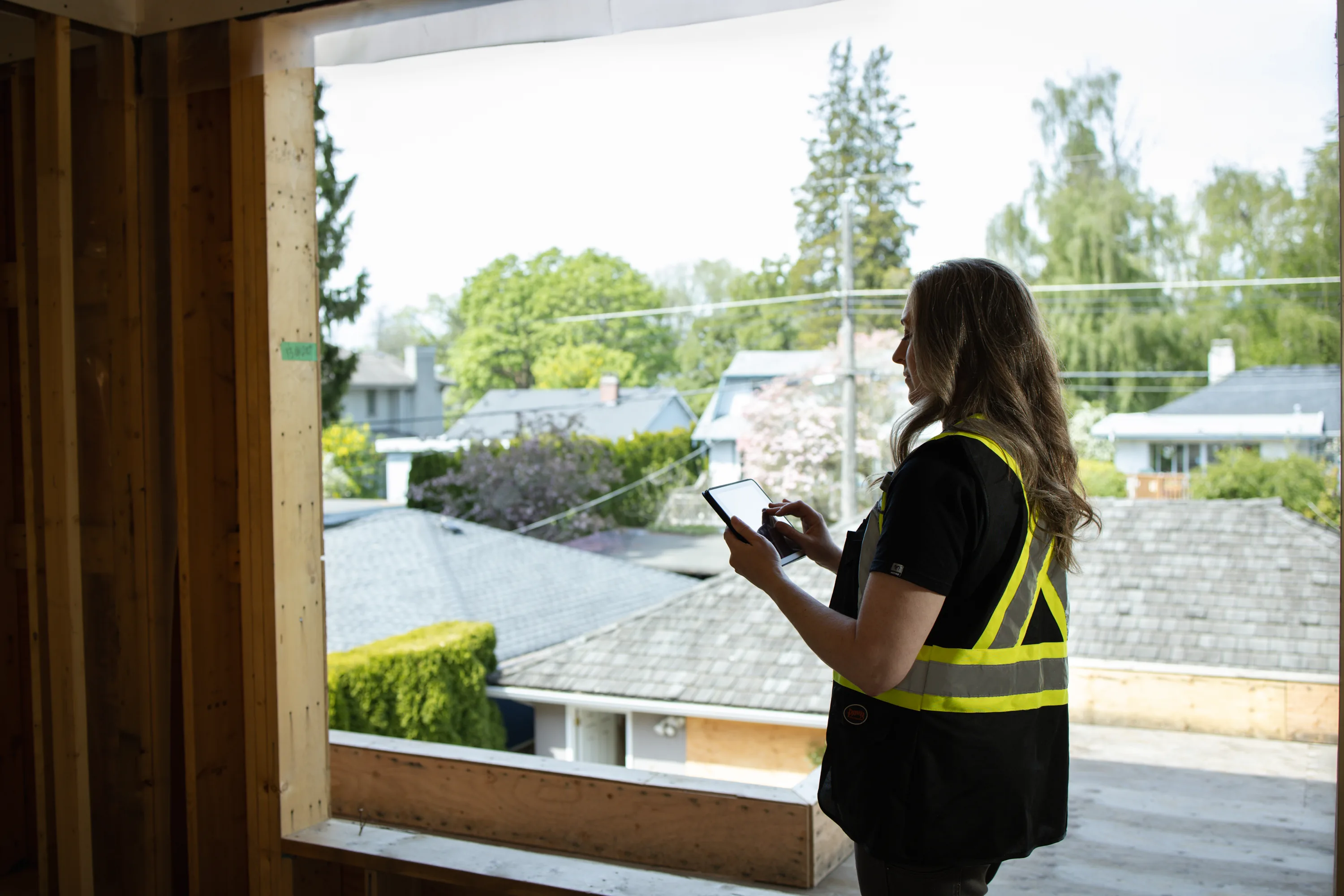 Rebecca Sorbara checking her phone by a large window overlooking a Vancouver neighbourhood at a building site