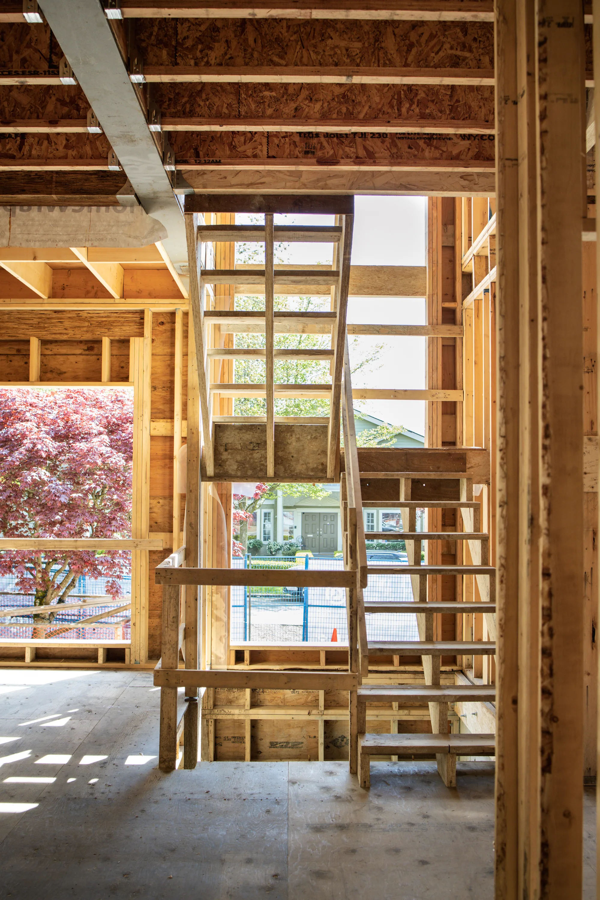 Interior wood framing and staircase of a home under construction with a cherry blossom tree visible outside